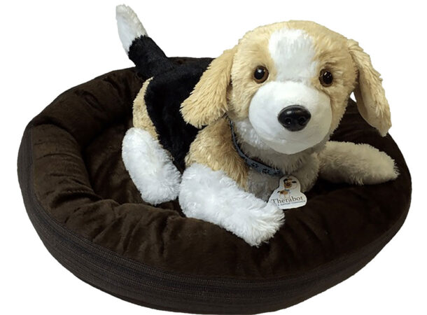 A stuffed robot dog lies on a brown dog bed. The brown, black and white robodog is looking at the reader.