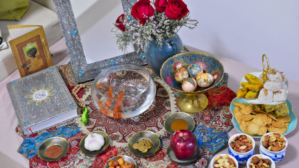 a table is colorfully decorated with items such as bowls of nuts, plates bearing an apple, coins, garlic and powders, as well as an ornate book and mirror