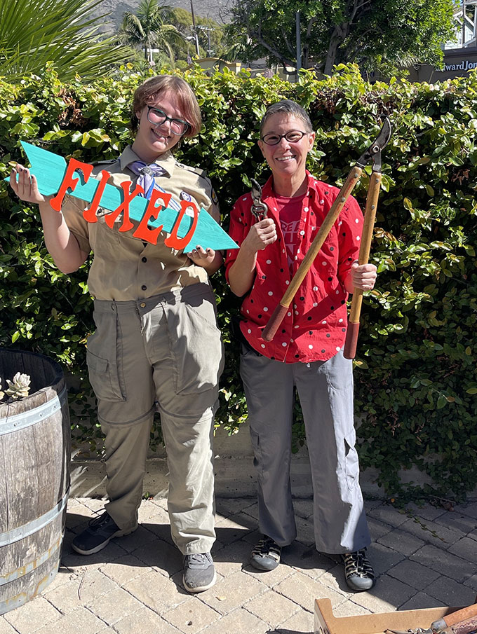 Two people standing outside on a sunny day. A young lady standing next to an older woman holding two sizes of pruning shears. Both are smiling and the young woman is holding a 'Fixed' sign.