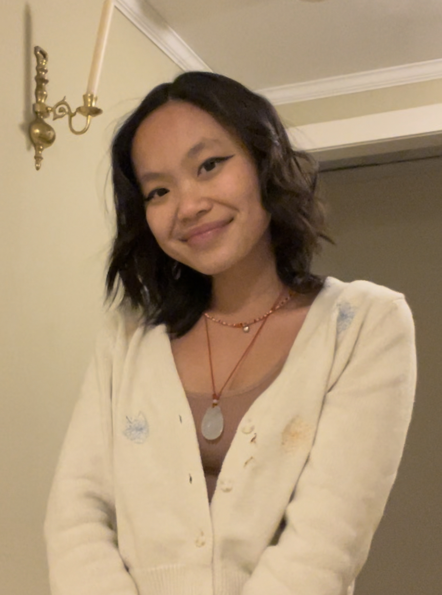 a teen girl with shoulder-length black hair, wearing a white sweater, smiles at the camera from beside a doorway