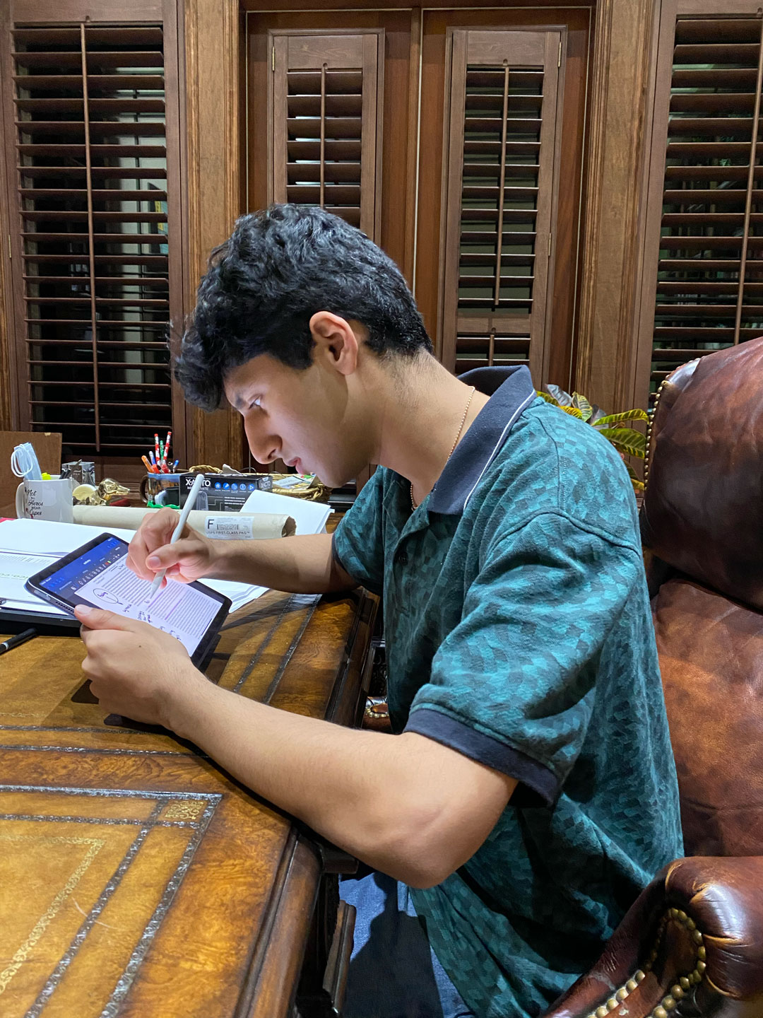 a teen boy sitting at a desk uses a stylus to write comments on a document displayed on a tablet computer