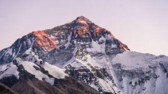a snow-dusted mountain is bathed in the pinkish light of dusk