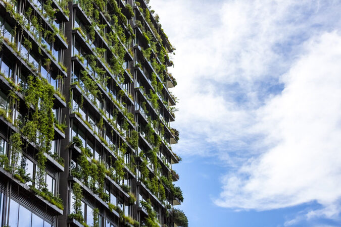 a photo of a high rise building with glass windows, draped in lush greenery
