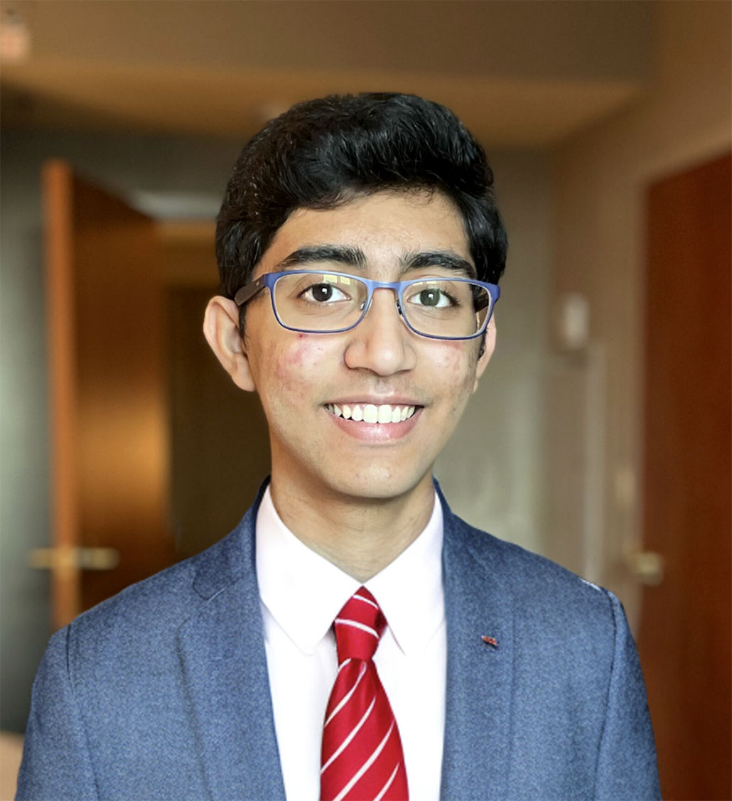 uma foto de Saathvik Kannan, um jovem de cabelos escuros, óculos, pele morena e um grande sorriso.  Ele está vestindo um terno cinza e uma gravata vermelha.