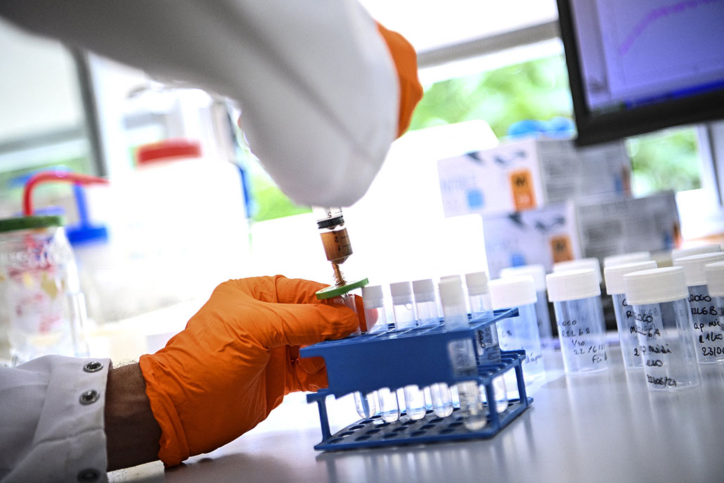 a pair of orange gloved hands is filling a vial with a solution on a laboratory counter