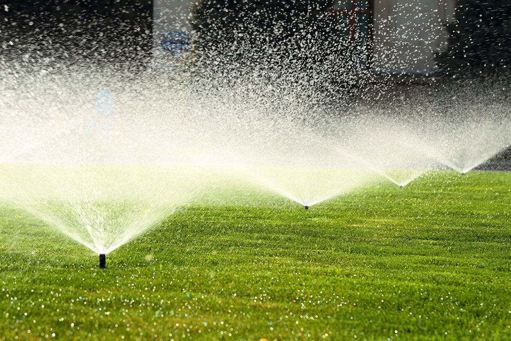 a photo of a yard with short, vibrantly green grass. Sprinklers dot the yard and are spraying the yard with water.
