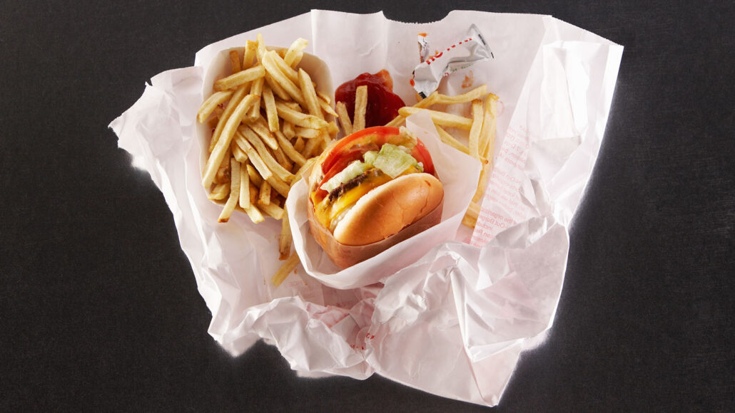 a hamburger, french fries and ketchup packets sit in an unfurled white paper fast-food wrapper