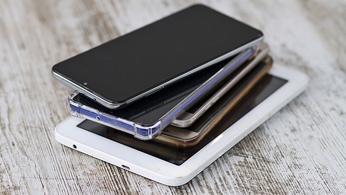 a photo of a handful of smartphones and tablets stacked on a wood surface