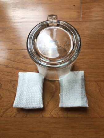 an upside down glass is placed on the floor; the rim of the glass holds the corners of two pieces of chocolate wrapped in paper towels, one dry and one wet
