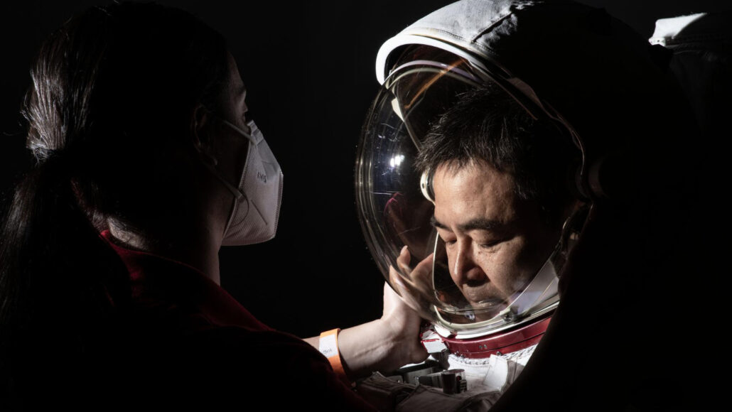 A photo of a woman putting a spacesuit helmet on astronaut Akihiko Hoshide.