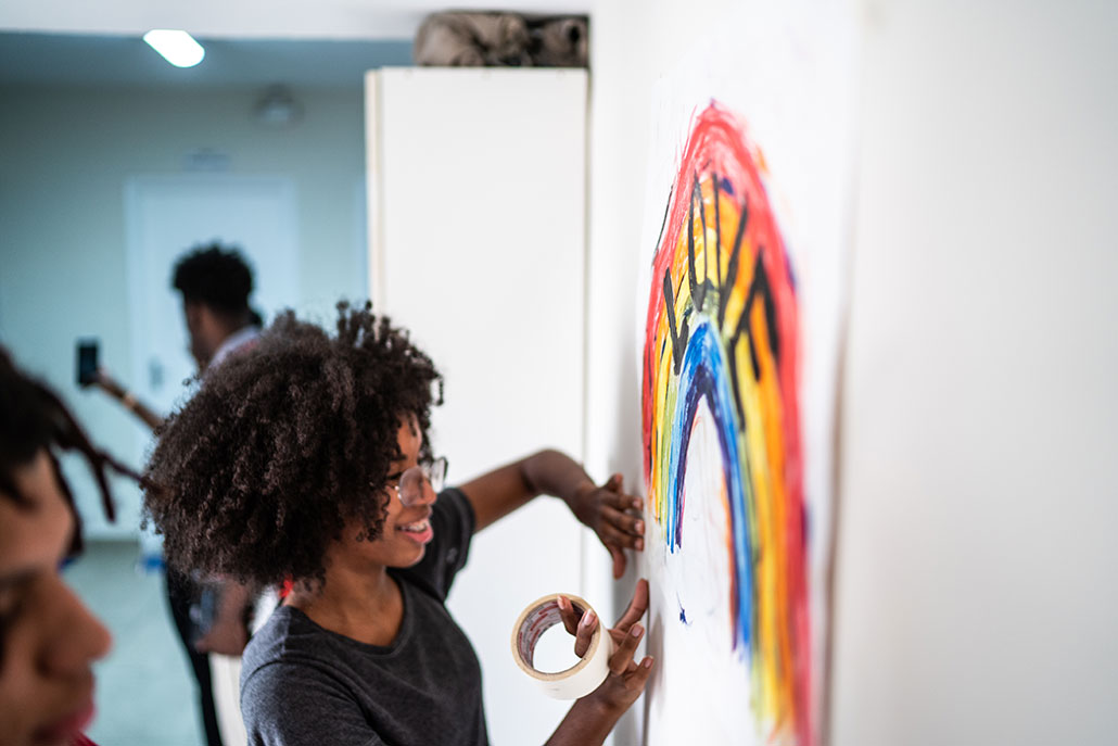 a photo of a young black girl painting a rainbow sign at school