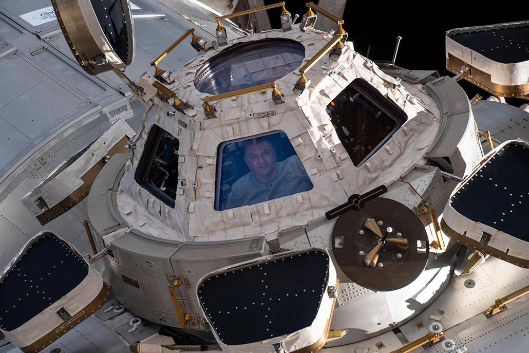 a photo of Kjell Lindgren peering out of one of the cupola windows on the International Space Station