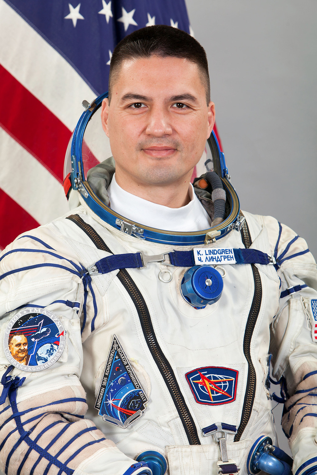 a formal photo of a white male astronaut wearing his spacesuit in front of an American flag