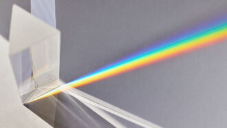 A top-down photo showing a triangular prism bending white light into the colors of the rainbow