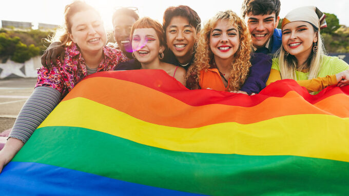 a photo showing a group of teens of different races and ages holding a Pride flag together
