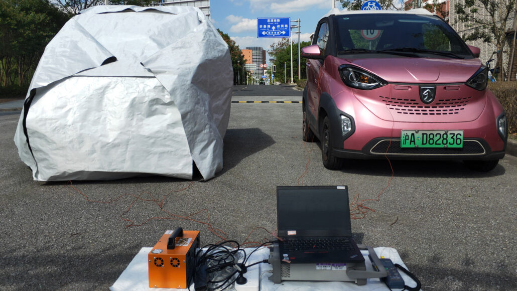 A photo of two cars parked next to each other. The car on the left is covered by a large white tarp that is wrapped around it while the car on the right is pink and exposed.