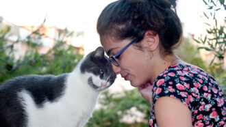 a pale woman with dark hair is being nuzzled by a black and white cat