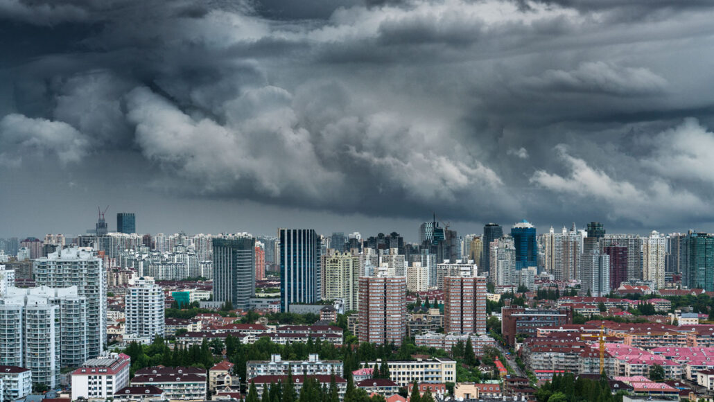 Heavy storm clouds loom over an urban landscape full of tall buildings