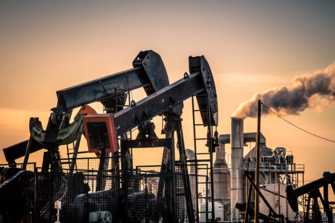 Two oil pumps stand in front of a cogeneration plant. Fumes rise out of the plant's exhaust pipe.