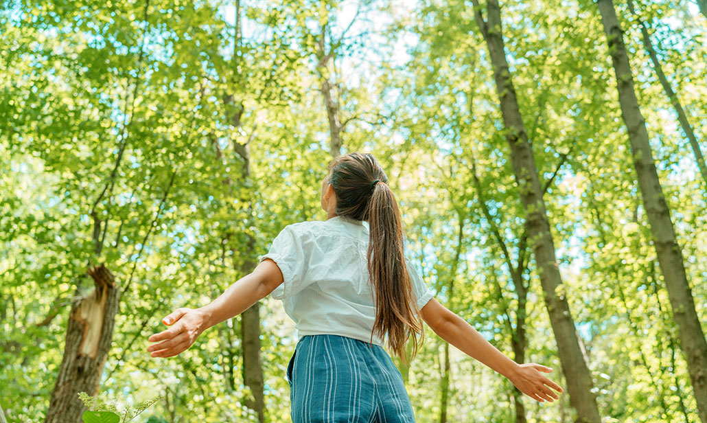 a young woman is standing outside looking up into the green trees surrounding her