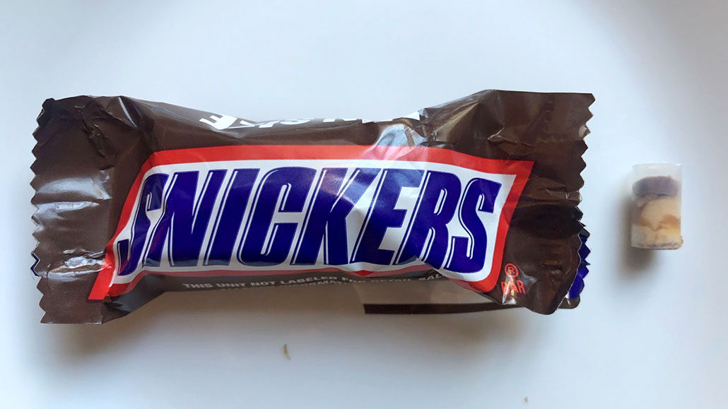 a wrapped fun-siz Snickers candy bar next to a candy core in a straw