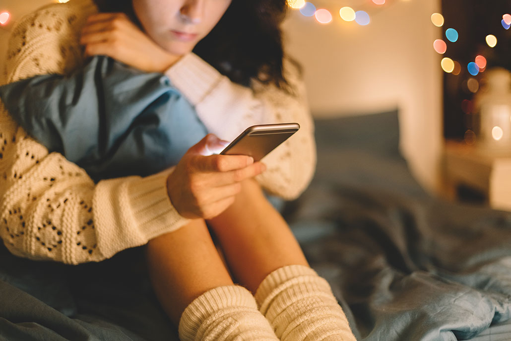 a girl sitting on a sofa, as seen from the nose down. she's grabbing her knees and looking at her phone