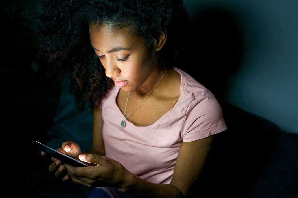 a young black woman with long curly hair on her phone in the dark