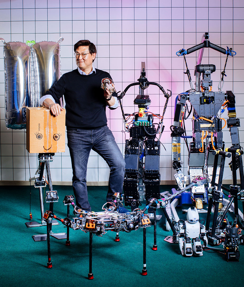 Dennis Hong standing with multiple robots and smiling