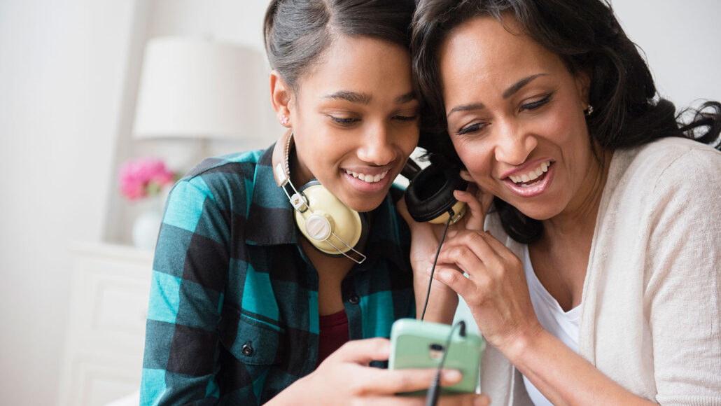 a Black teens is sharing her headphones with her mother, they are both listening and smiling