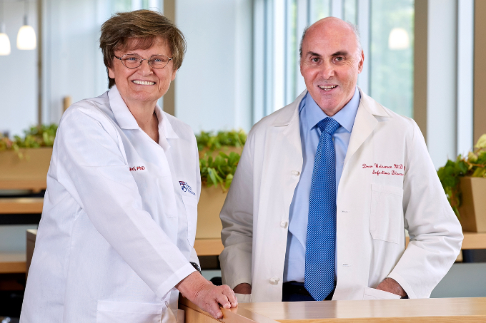 Katalin Karikó and Drew Weissman standing next to a table wearing lab coats