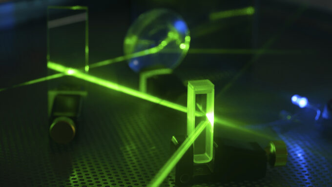 A photo of a green laser beam being sent through several pieces of glass.