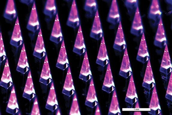 Rows of microscopic needle tips are lit up by a purple and pink light.