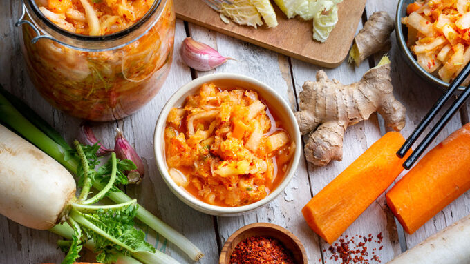 a table with ingredients for kimchi scattered across it, a jar of kimchi is in the upper left