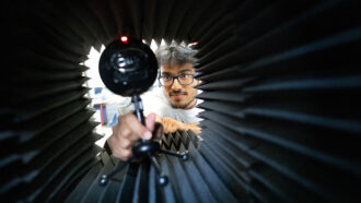 a photo of Yash Wani, a brown skinned man with short hair and glasse, positioning a microphone from the inside of a black tube