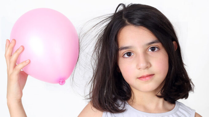 a pale girl with shoulder length hair is holding a pink balloon near her head. The hair closest to the balloon is floating towards the balloon.