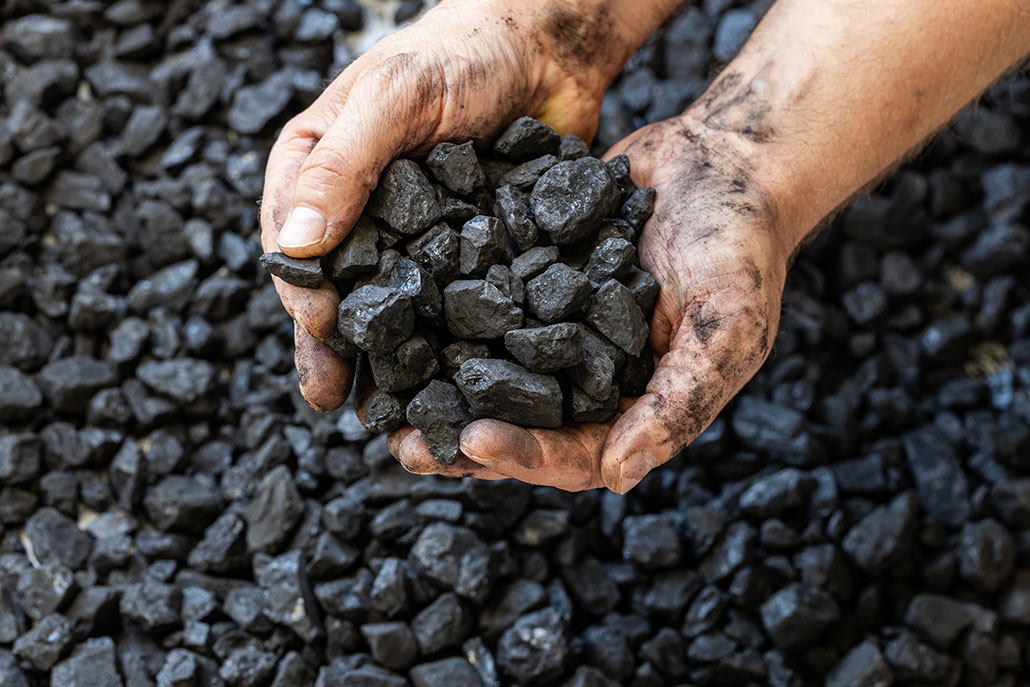 hands holding coal above a pile of coal