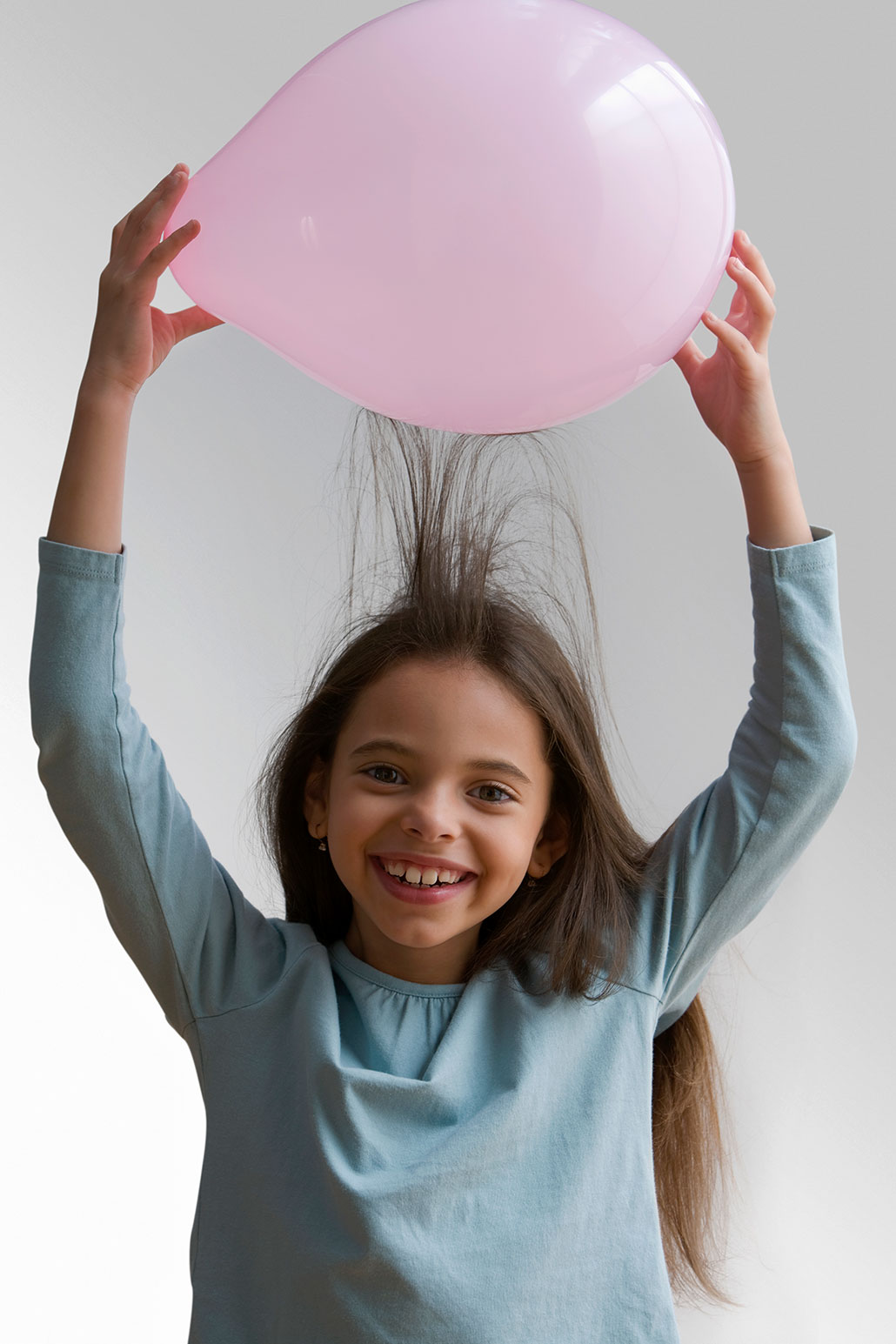 a girl holding a pink balloon above her head showin ghow it makes her hair stand up