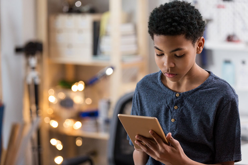 a kid with short black curly hair, brown skin, and a blue shirt is watching a tablet held in his hand