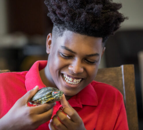 a teen boy smiles as he gently holds up his pet turtle