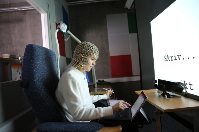 a student writing with a pen or typing with electrodes on head