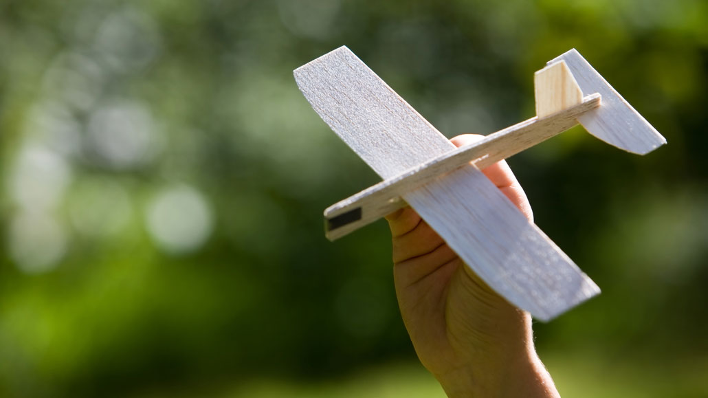 a hand holding a simple balsa wood toy airplane