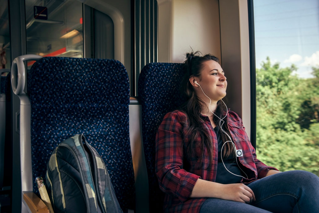 a woman smiles and looks out a train window while listening to music