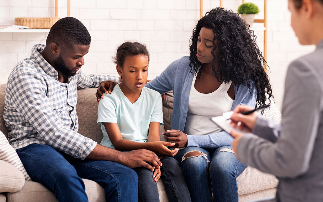 a young Black girl sitting on a couch flanked by her parents at a therapy appointment