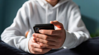 a photo of a kid in a white hoodie holding a smartphone. They are sitting cross-legged, the photo only shows their torso and hands.