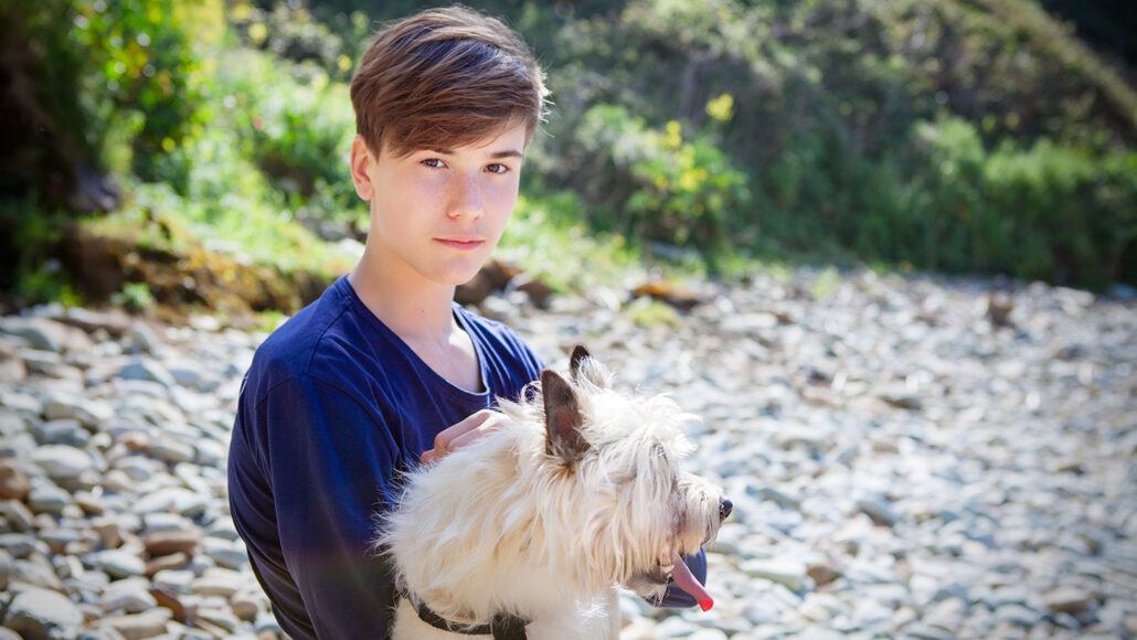 a boy holding a fluffy white dog outside