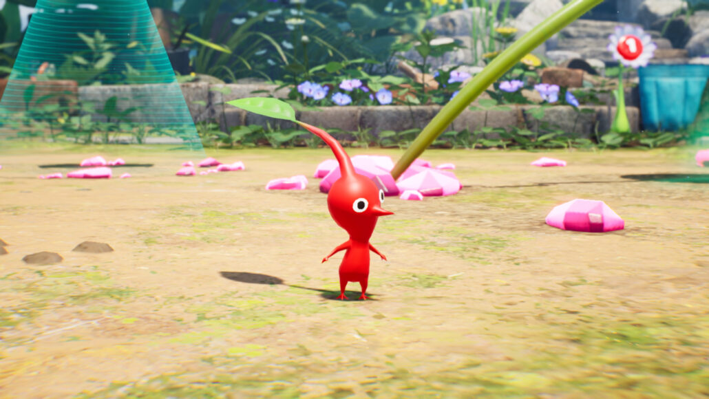A red Pikmin is standing on the ground. A single green leaf sprouting from a long thin stalk on its head. Garden plants and flowers stand behind a brick wall in the background.