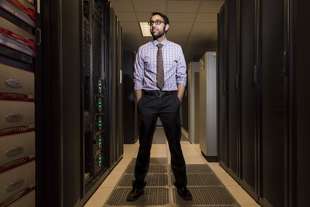 a photo of Vijay Gadepally, a man with black hair and light brown skin wearing business clthes, standing in a data center