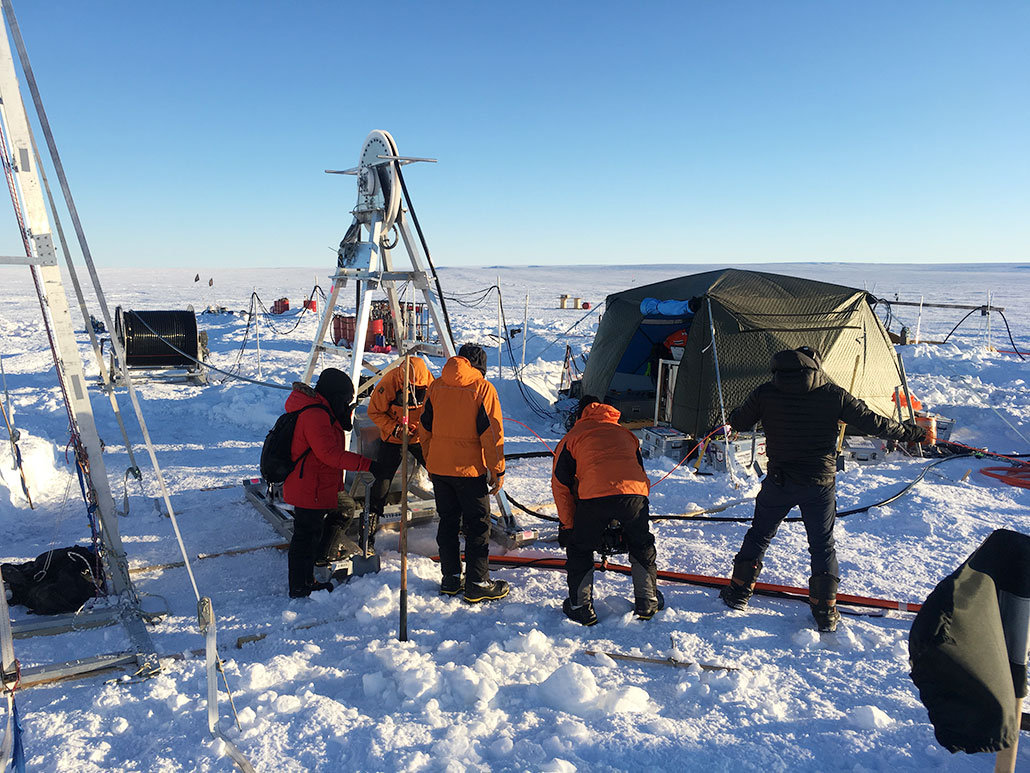 workers in action, melting a hole through an ices shelf next to tents and other equipment