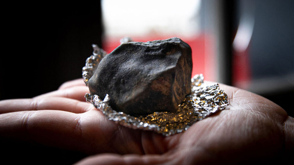 a dark rock about the size of a tennis ball sits atop a piece of foil on an open palm