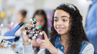 A teen girl in a classroom holds up a plastic model of a molecule